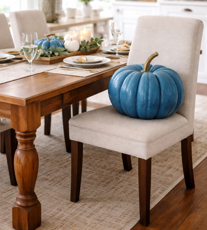 A blue pumpkin resting on a white dining chair beside a wooden table